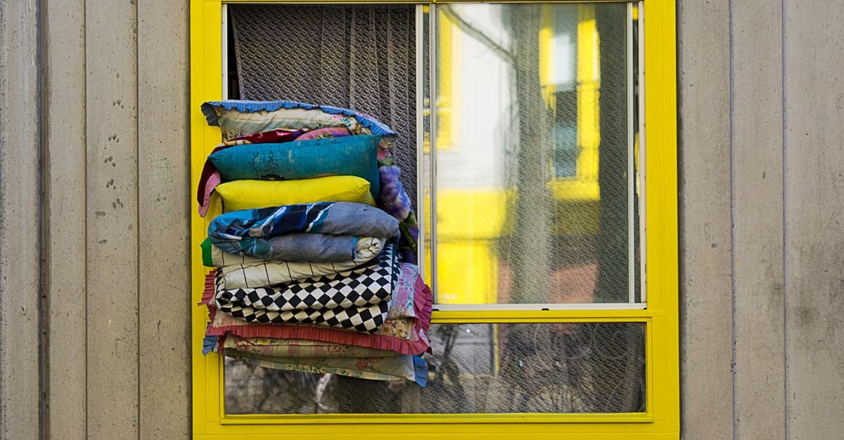 Stack of brightly coloured outdoor cushions resting against a yellow painted wall