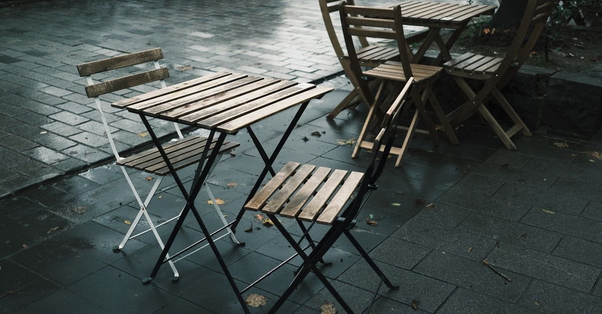 Empty wooden tables and chairs standing in the rain on a wet street