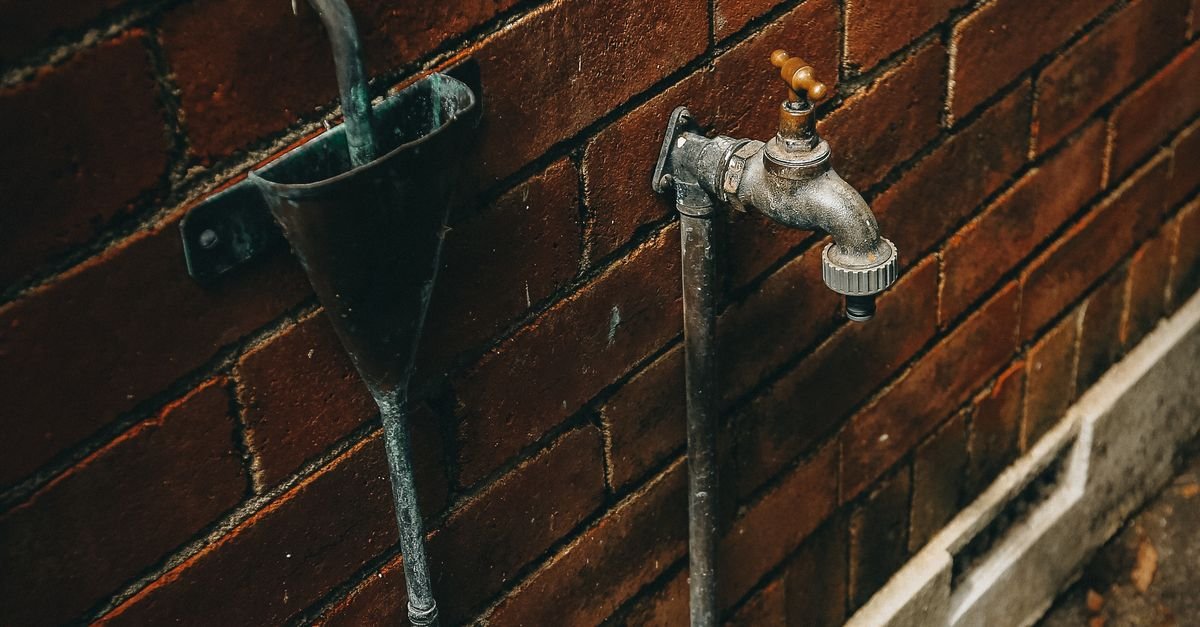 Weathered outdoor tap mounted on a brick wall, ready for a jet washer inlet hose