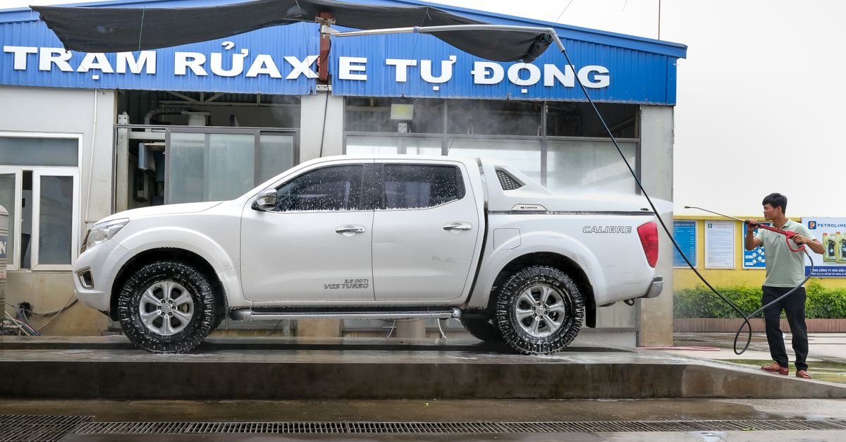 Person using a jet washer lance to rinse a white pickup truck at an outdoor wash bay
