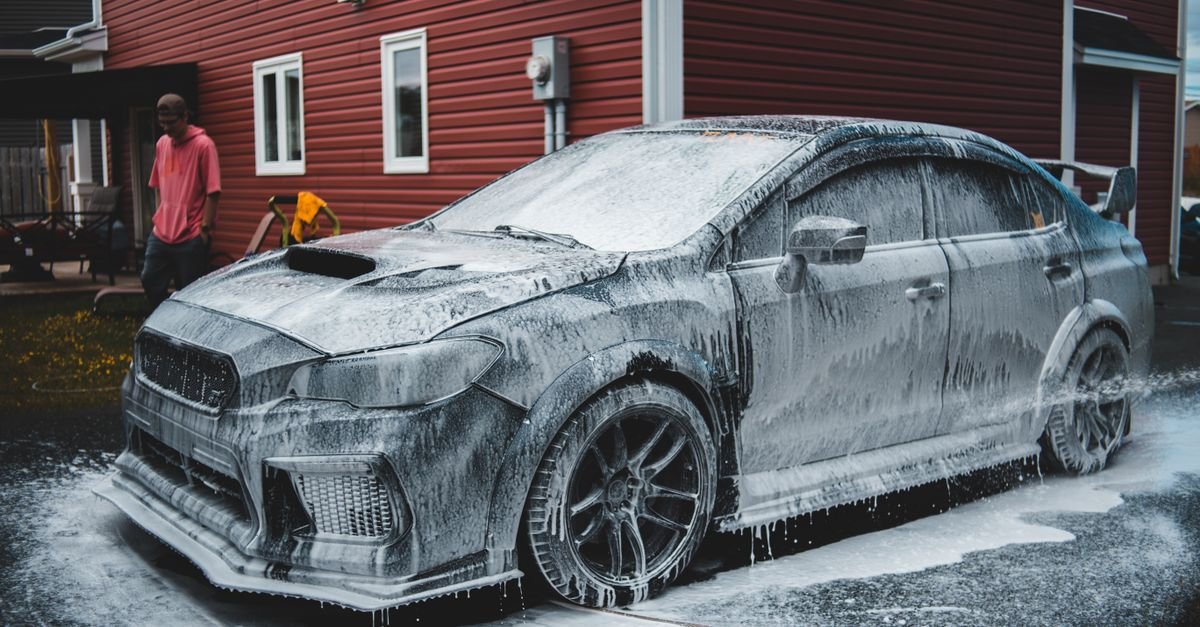 Car covered in thick cleaning foam at an outdoor wash bay while the operator waits for it to dwell