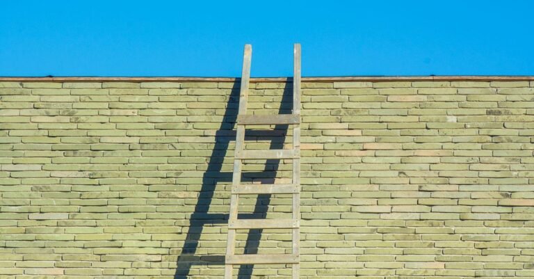 A wooden ladder leaning against a tall brick wall under a clear blue sky