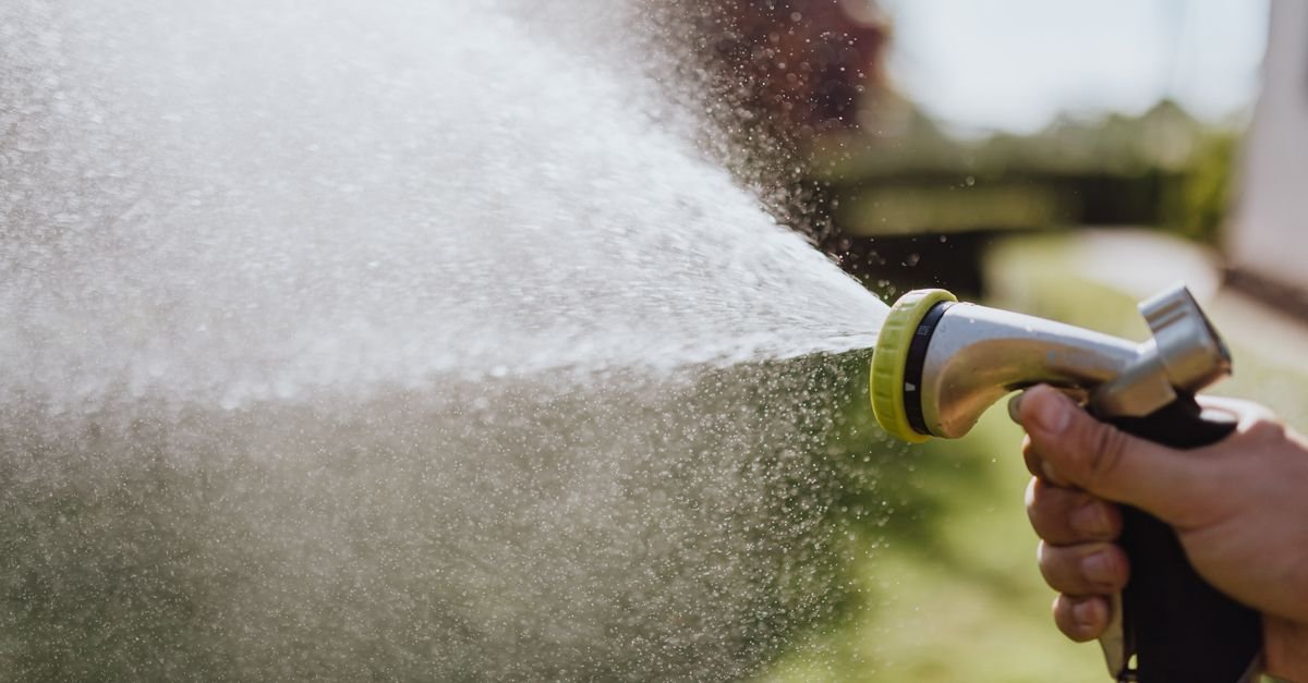 A hand holding a hose nozzle, the water stream breaking up into spray a short distance from the tip