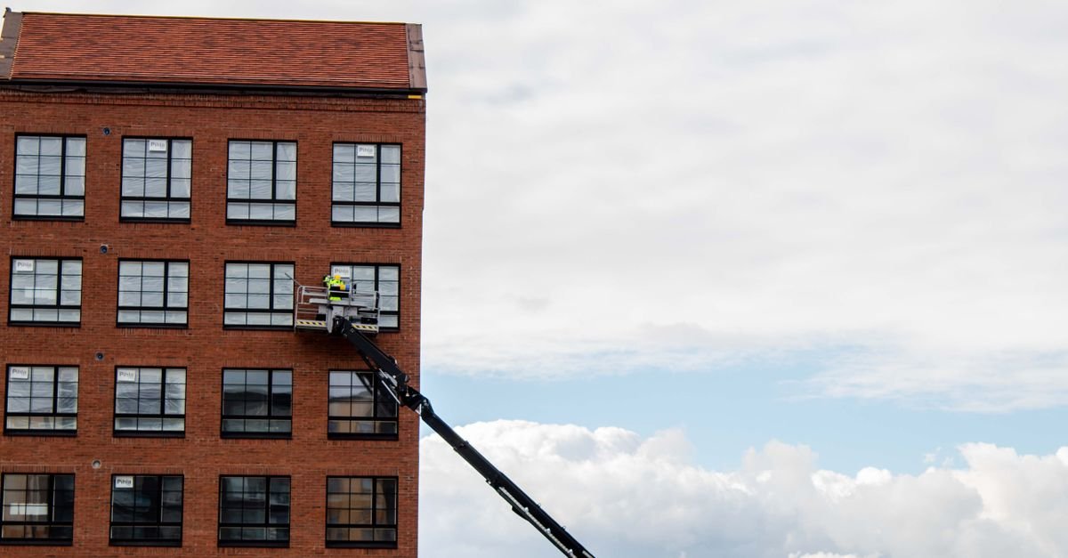A worker on a telescopic lift platform working at roofline height against a brick building