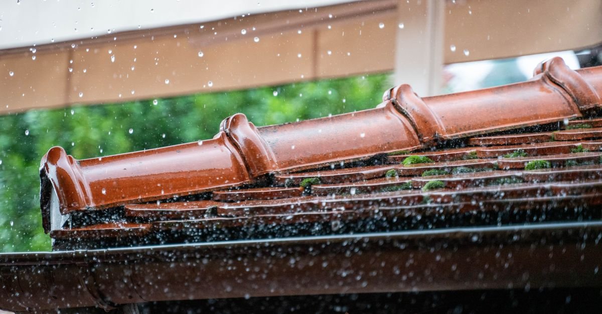 Rainwater running off the edge of a terracotta tiled roof in heavy droplets