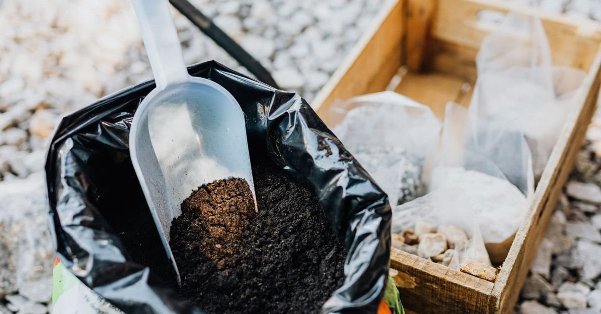 A plastic garden scoop with a squared leading edge and raised sides resting beside potting soil