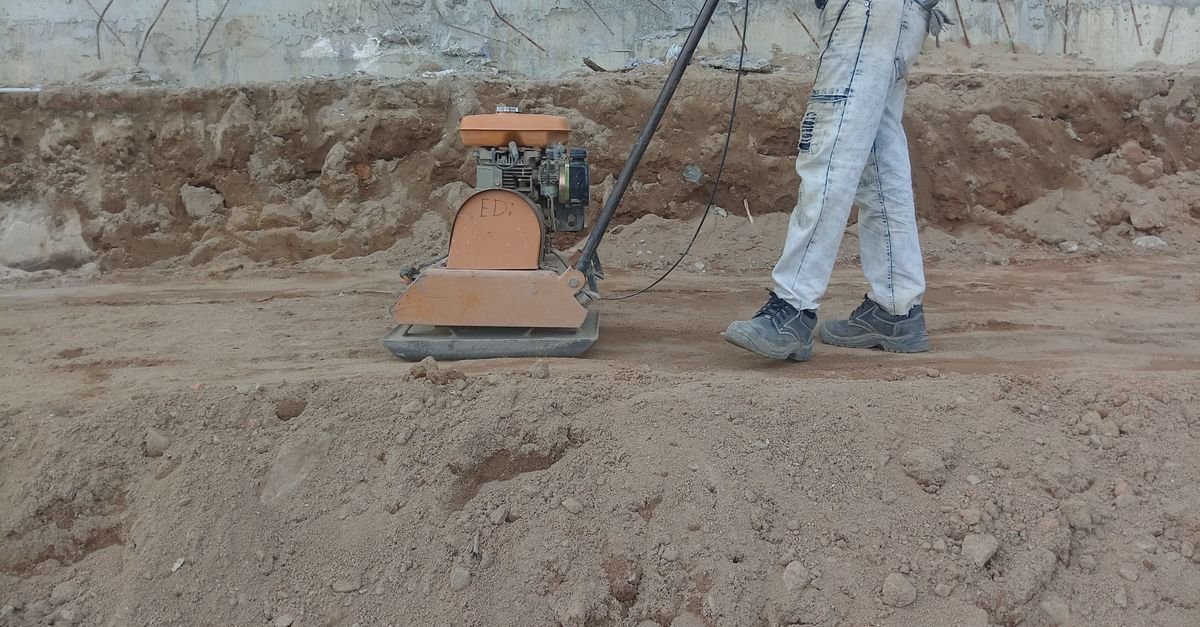 A construction worker running a vibrating plate compactor over ground outdoors