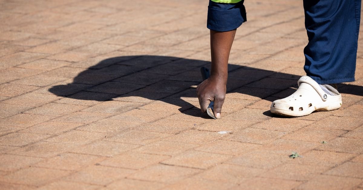 A worker in uniform working a hand tool along the joints of an outdoor brick pathway