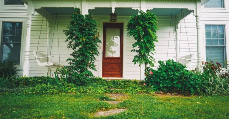 Covered front porch of a white house with plants, hanging swings and a painted timber floor