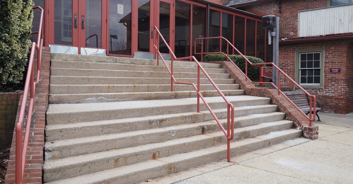 Concrete steps with metal handrails leading up to the entrance of a red-brick building