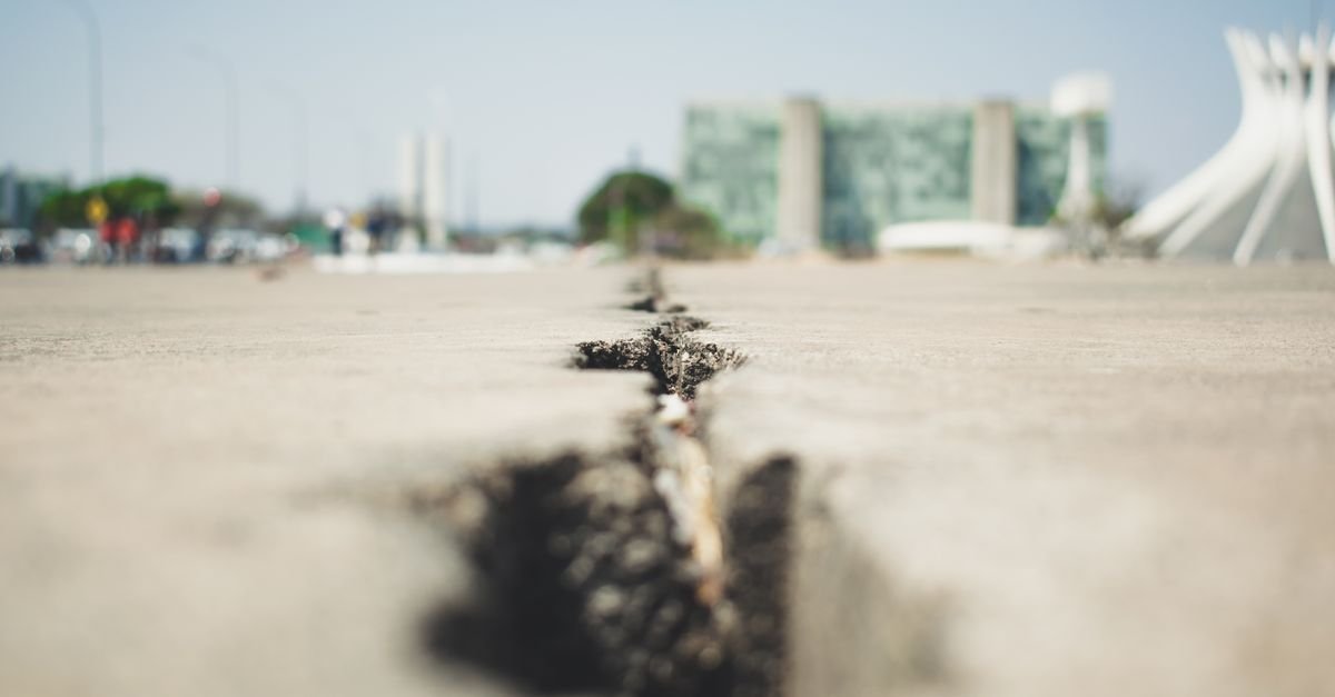 A close-up of a cracked pavement surface with city buildings blurred in the background