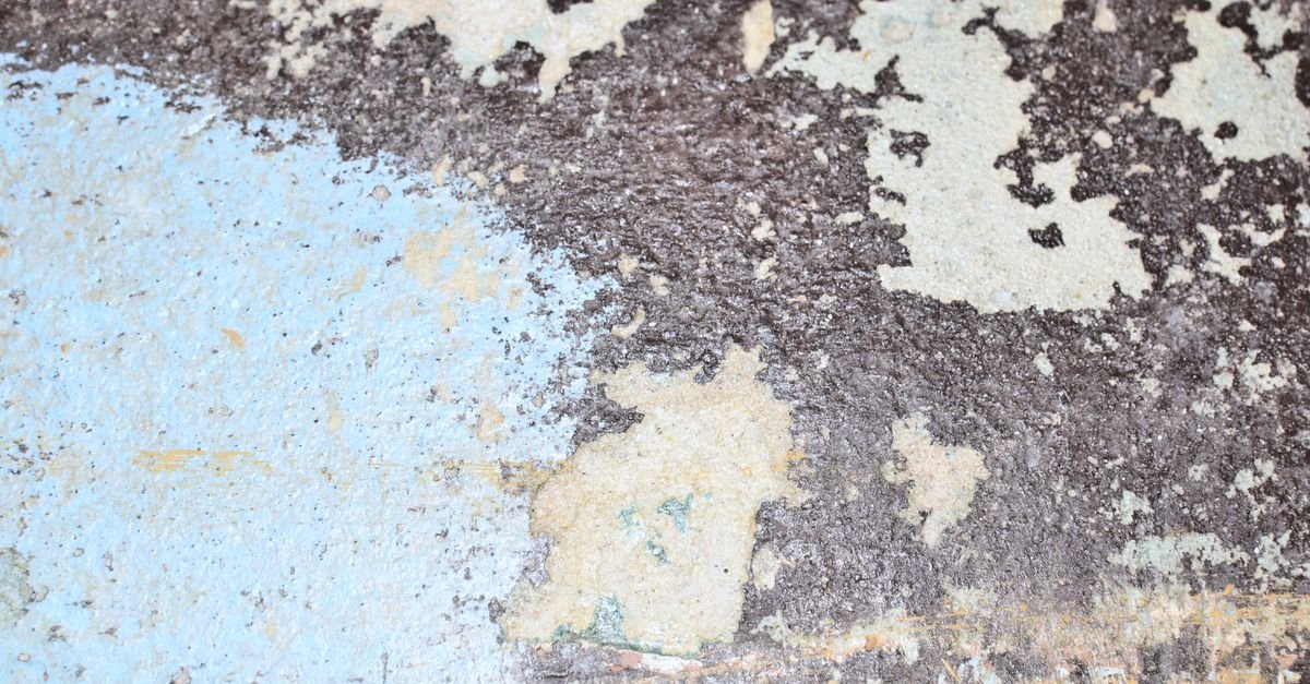 An aged stone surface with corrosion and peeling black paint, a mechanically bonded coating that no chemical will simply switch off