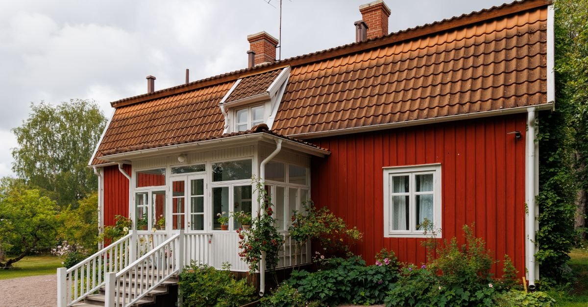 A red-painted wooden house with white trim, a gable end and a deep roof overhang above the wall