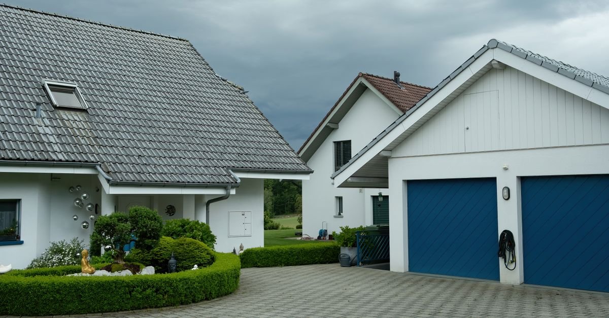 Suburban houses with blue garage doors under a flat, overcast sky with greenery around them