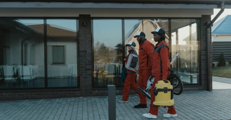 A uniformed cleaning crew carrying equipment towards a glass-fronted house before starting an exterior wash