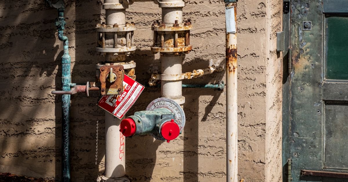 Rusted outdoor pipework with pressure gauges and a warning sign, the kind of system an unloader protects from a spike