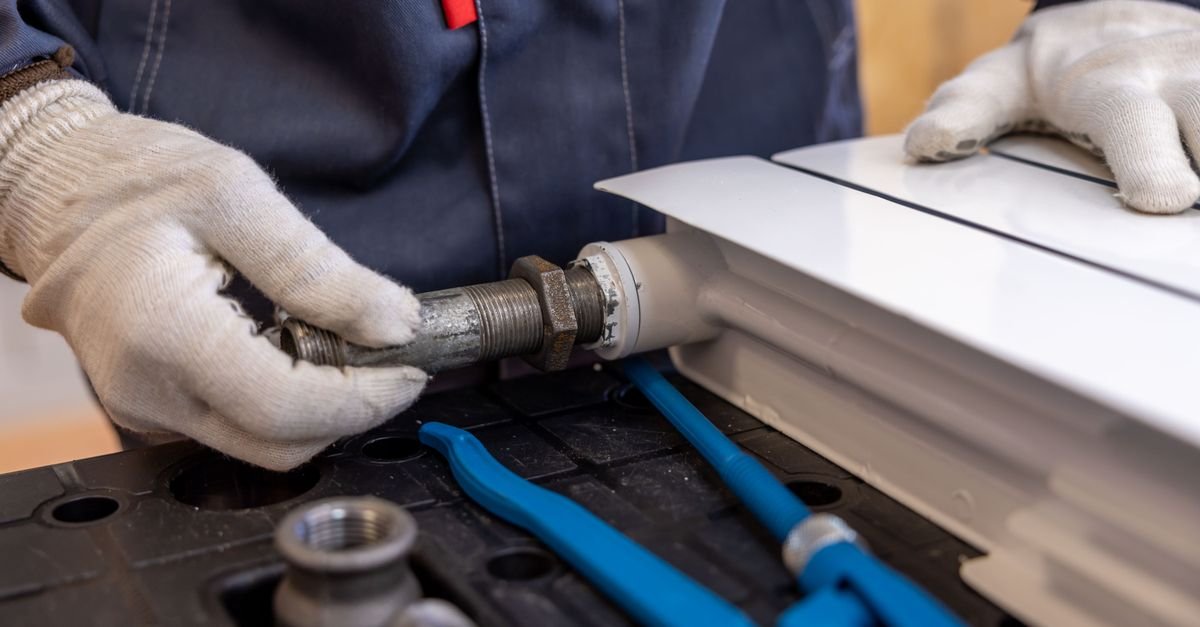 A tradesperson using a purpose-made wrench on a threaded pipe fitting, the correct tool for backing an unloader out of a pump head