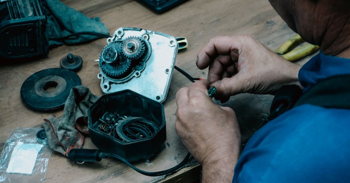 A technician stripping a small mechanical assembly down on a bench, parts laid out in the order they came off