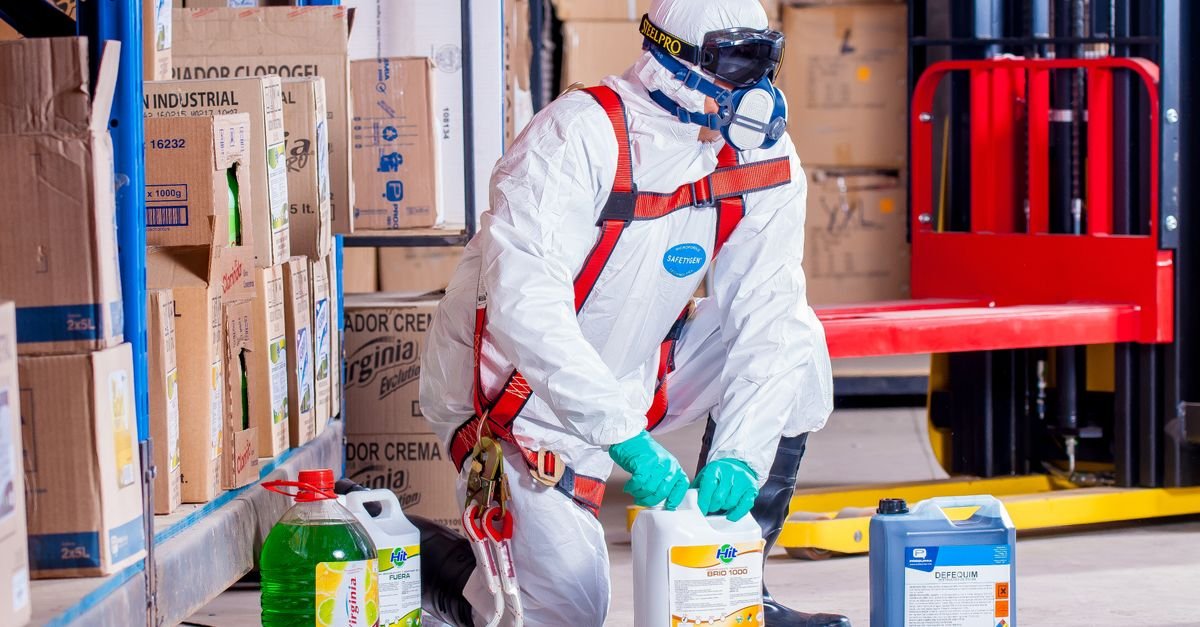 Worker in protective gloves and goggles handling chemical containers in a storage area