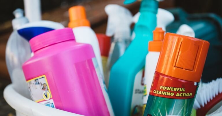 Assorted detergent bottles and spray cleaners standing in a bucket on an outdoor step