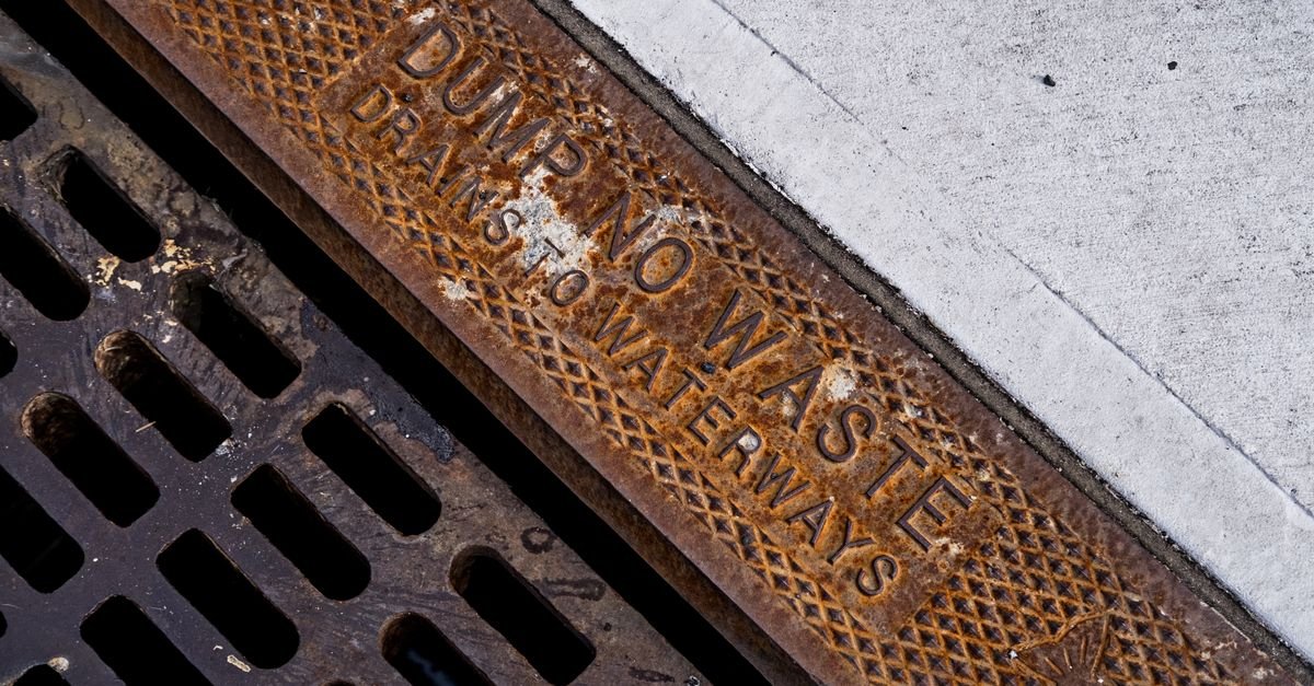 Rusty metal storm drain grate on a pavement with an environmental warning cast into it