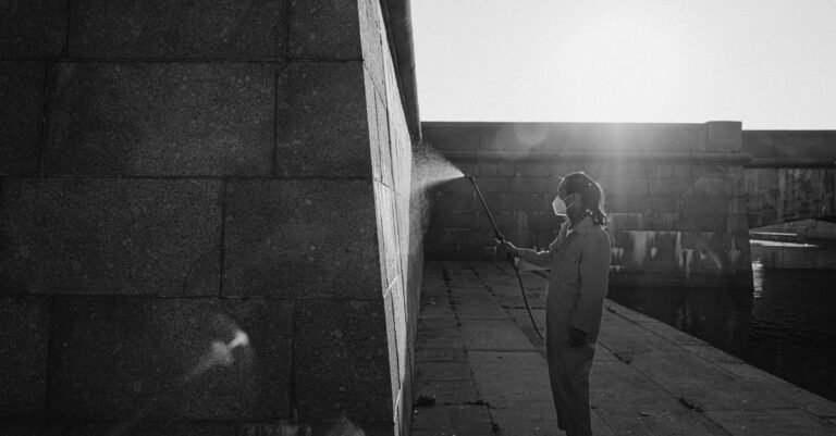 A worker in a jumpsuit power washing a wall with the spray held level rather than angled upward