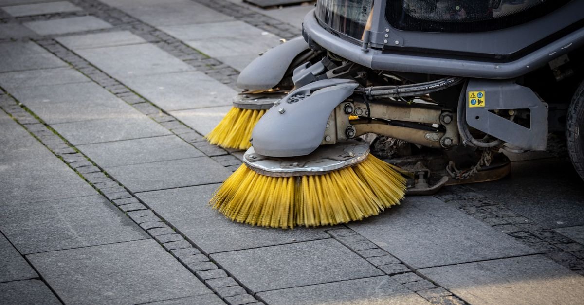 Close-up of a wide rotating sweeper brush working across a paved street surface