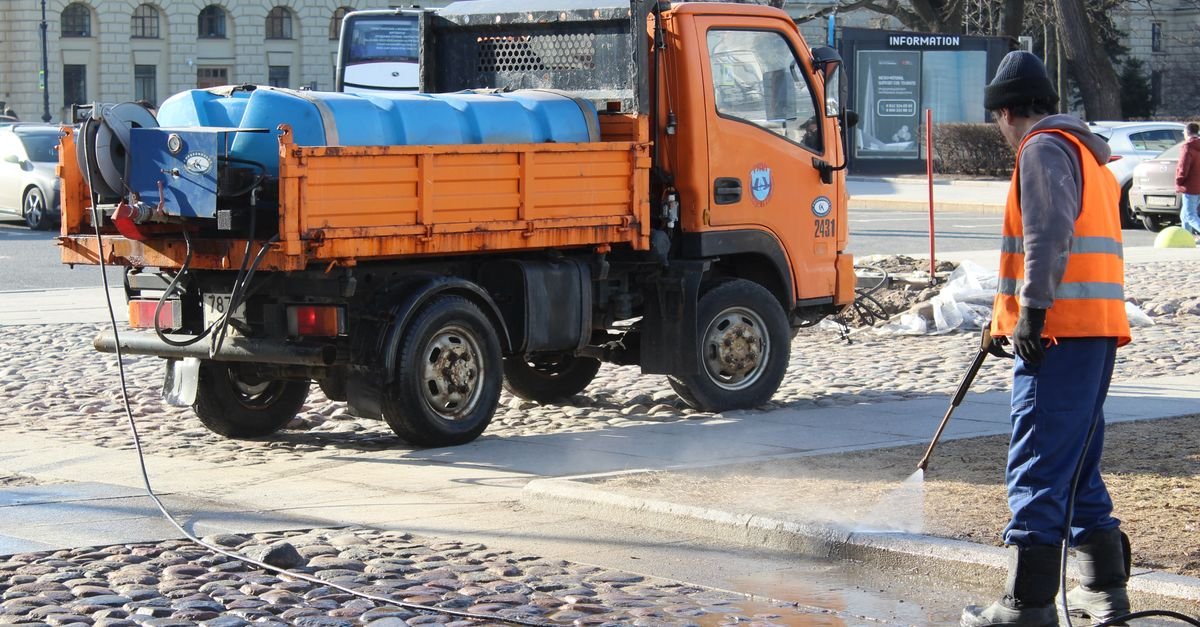 A city worker cleaning a cobblestone street by hand with a high-pressure hose
