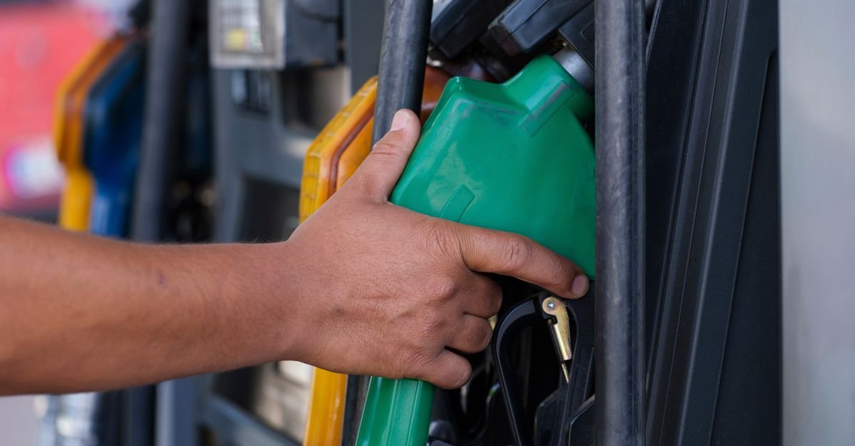 A hand holding a fuel pump nozzle at a filling station