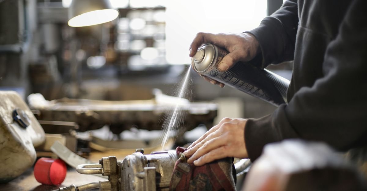 A person cleaning a machine part with an aerosol spray can in a workshop