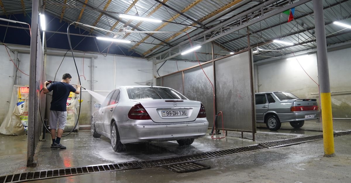 A man using a pressure washer to clean a silver car at night, the running machine where a gravelly pump note first shows up