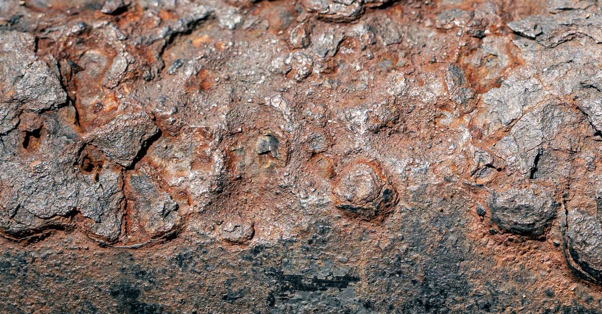Close-up of a corroded iron surface covered in fine pitting, the cratered texture cavitation erosion leaves on a valve seat