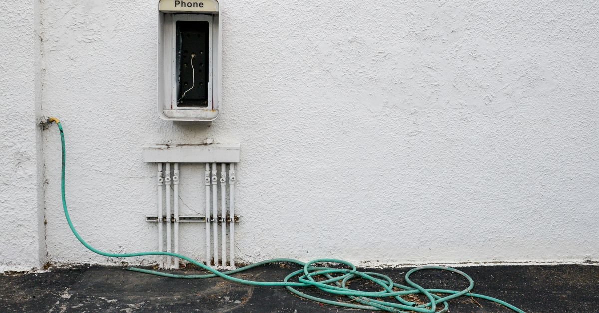 A long hose coiled on a wall-mounted reel against a weathered white wall