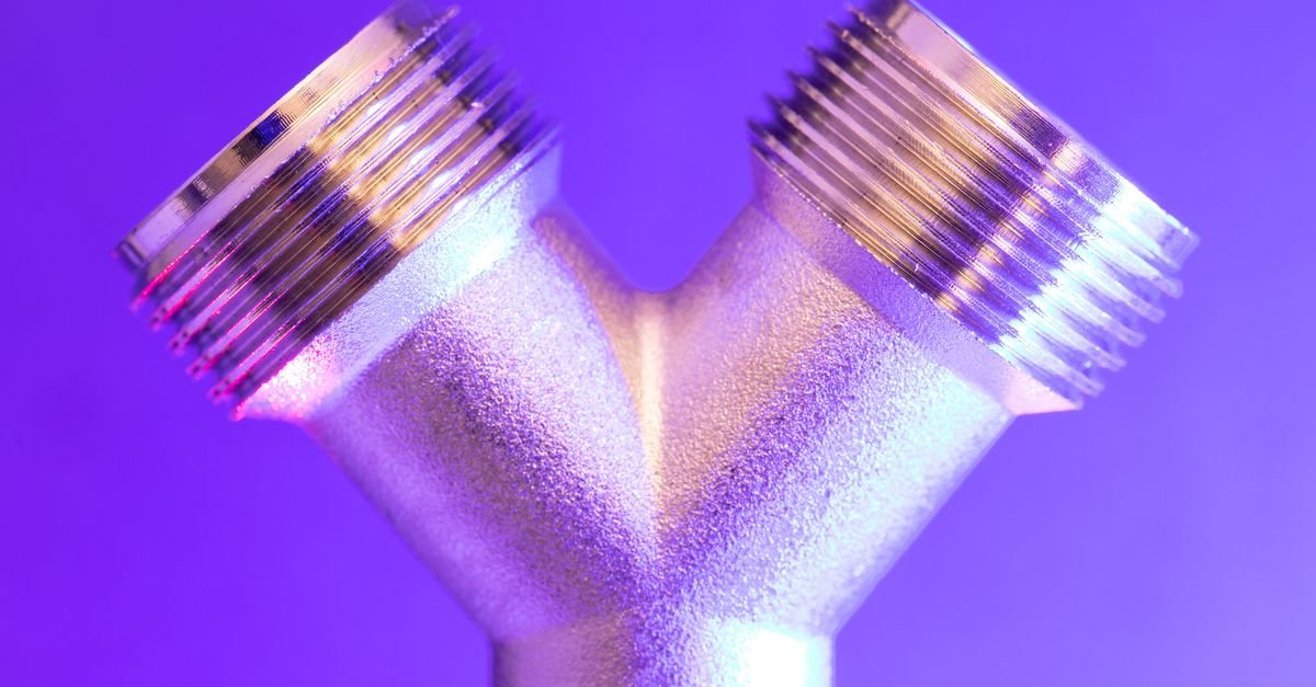 Close-up of a polished metal pipe section lit from the side, the kind of inline body a chemical injector is machined from