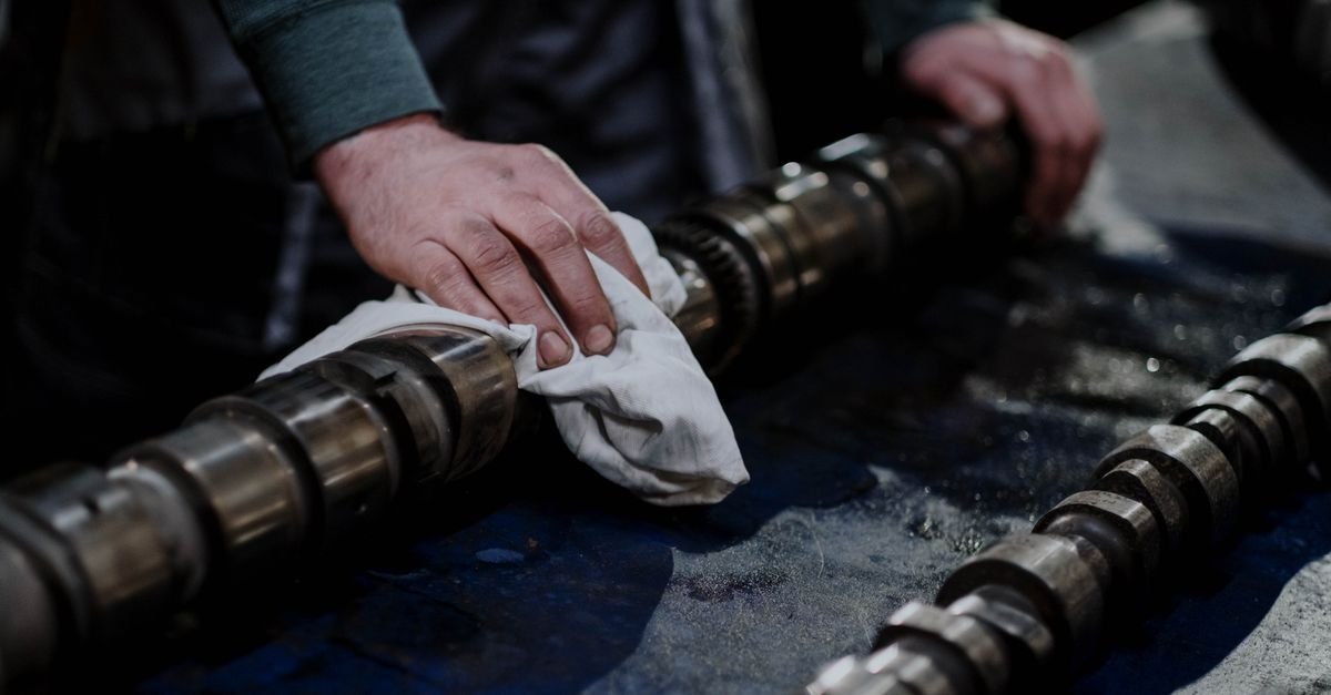 Close-up of a mechanic cleaning a metal machine component with a cloth on a workbench
