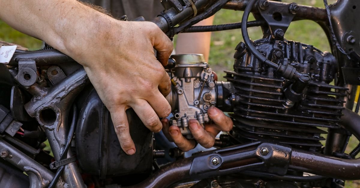 A mechanic's hands working at the top end of a small petrol engine outdoors, the position you are in when clearing a flooded cylinder