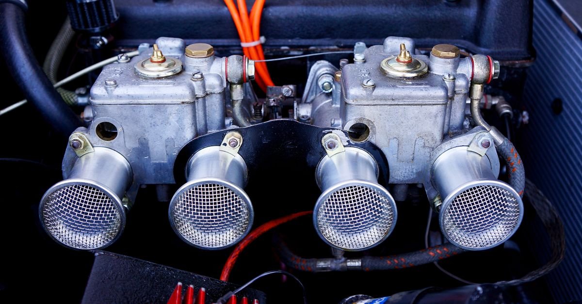 A pair of carburettors in an engine bay, showing the fuel bowls whose float needles are supposed to shut the supply off when the engine stops