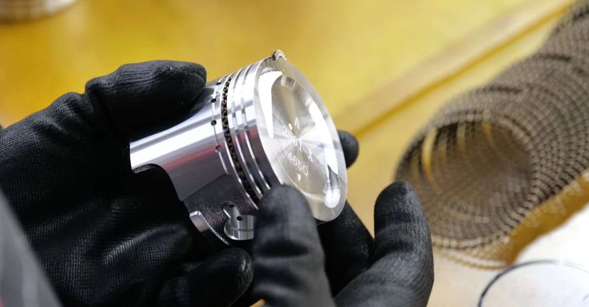 Gloved hands examining a metal engine piston closely on a workbench, the kind of slow inspection a cold pump needs before anything is switched on