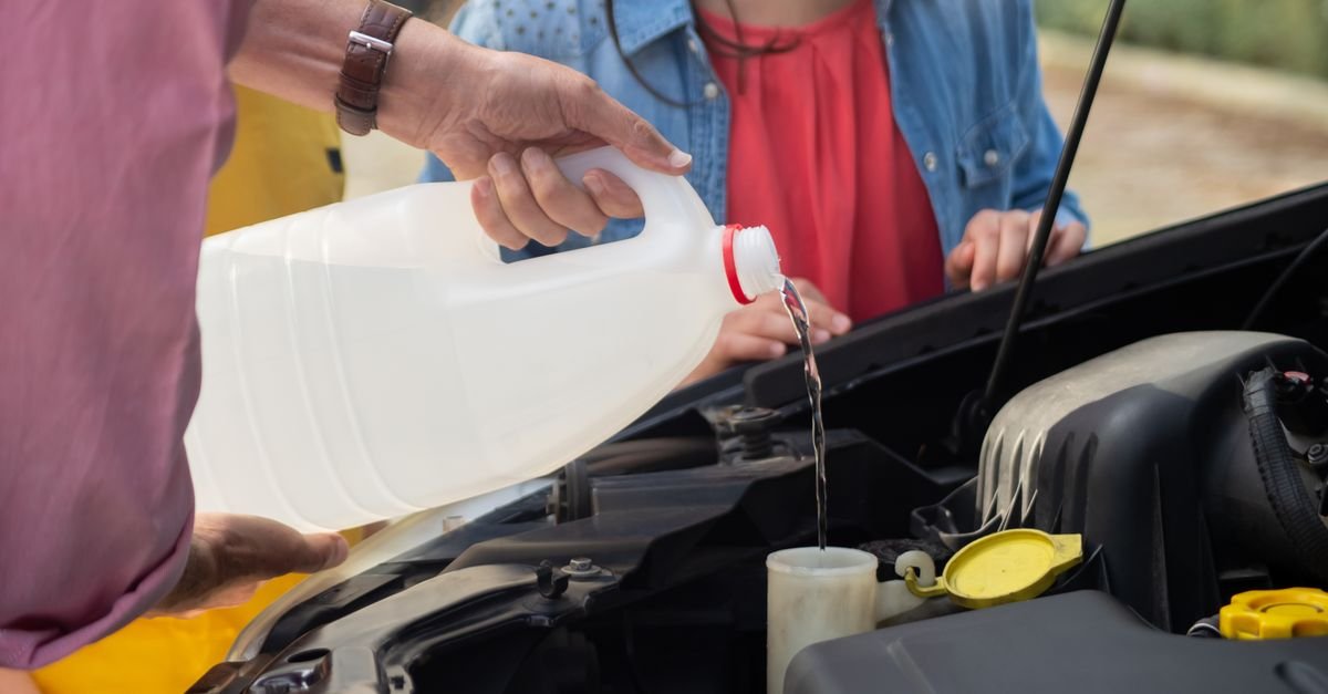 A person pouring fluid from a bottle into a machine's fill point, the thirty seconds of work that prevents a frozen pump entirely