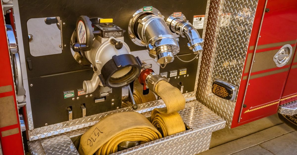 Close-up of threaded high-pressure hose couplings and connection fittings on the side panel of a fire truck
