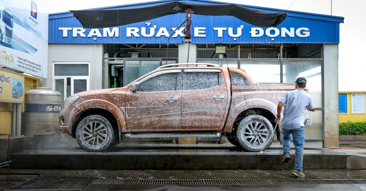 Man holding a pressure washer gun to rinse soap foam off a pickup truck at an outdoor wash bay