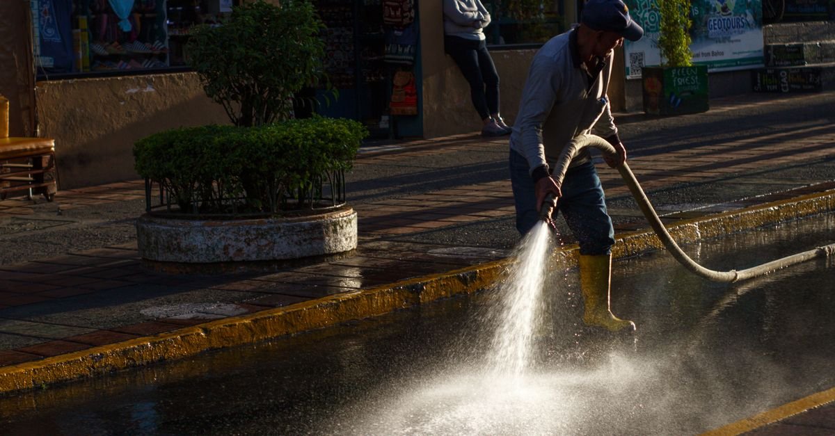 City worker bracing against the spray while cleaning a street with a high-pressure hose at dusk