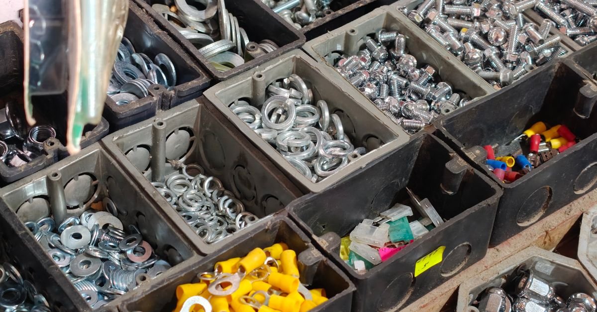 Sorted storage bins of small hardware including nuts, bolts and rubber washers on a workshop shelf