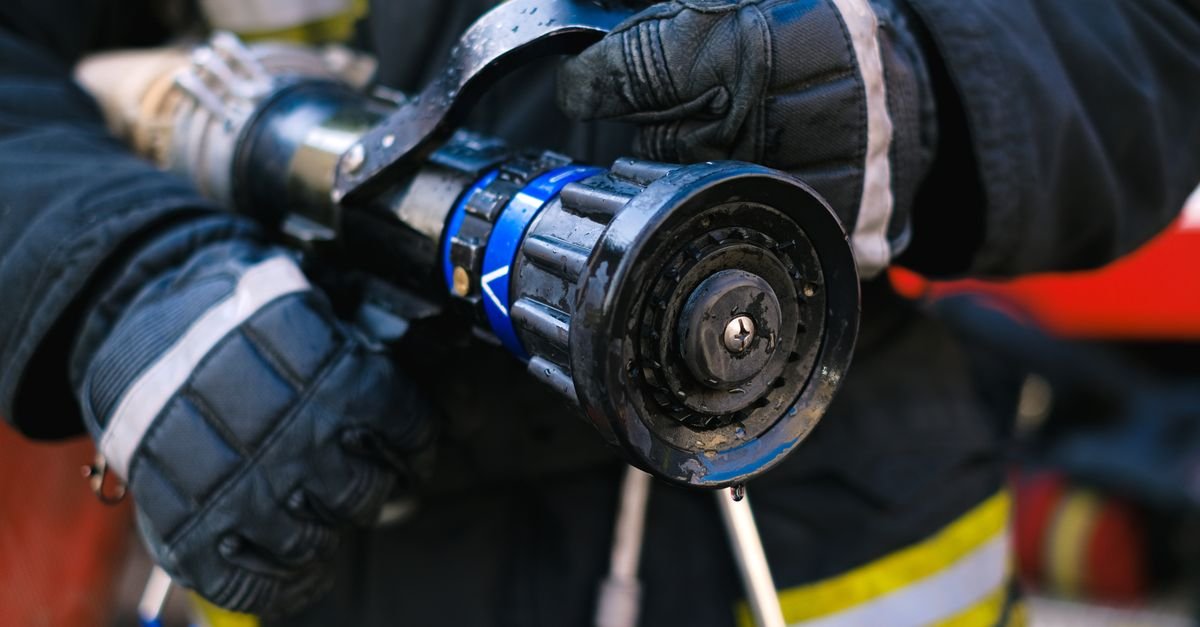 Gloved hands braced on a high-pressure hose nozzle, the two-handed grip that keeps a live jet under control