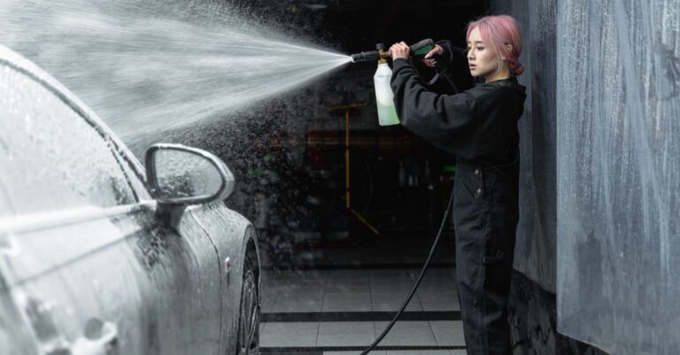 Person gripping a pressure washer trigger gun with both hands while rinsing foam off a car inside a garage