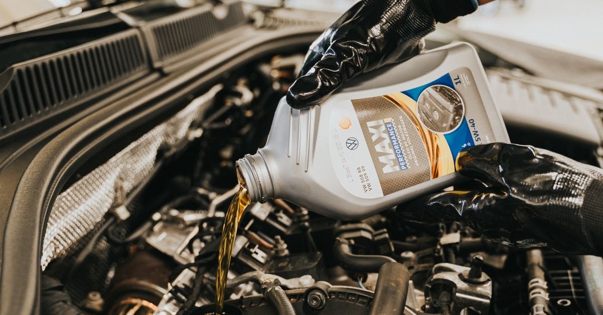 A gloved mechanic pouring fresh engine oil, the grade of which sets how hard the engine is to crank on a cold morning