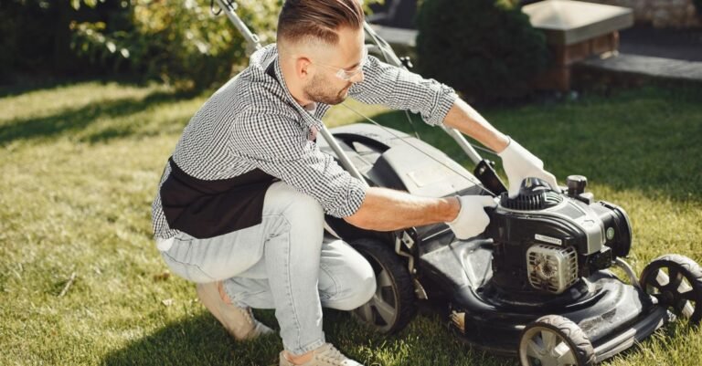 A man crouched beside a small petrol engine in a sunny garden, preparing it for work