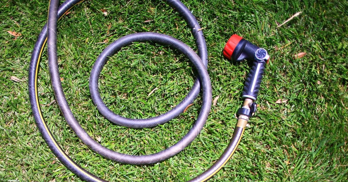 A garden hose left tightly curled on grass, the kind of restricted inlet run that starves a pressure washer pump and lets air in