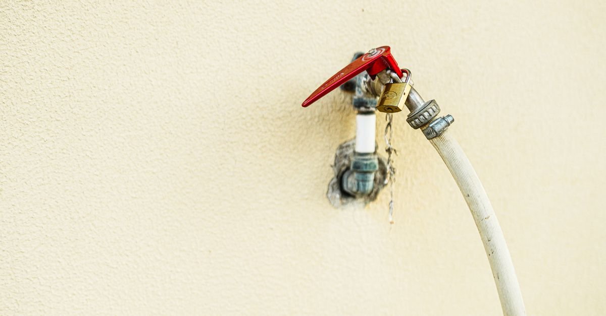 An outdoor water faucet with a bright red handle mounted on a wall, the first thing to open fully when a pressure washer will not build pressure