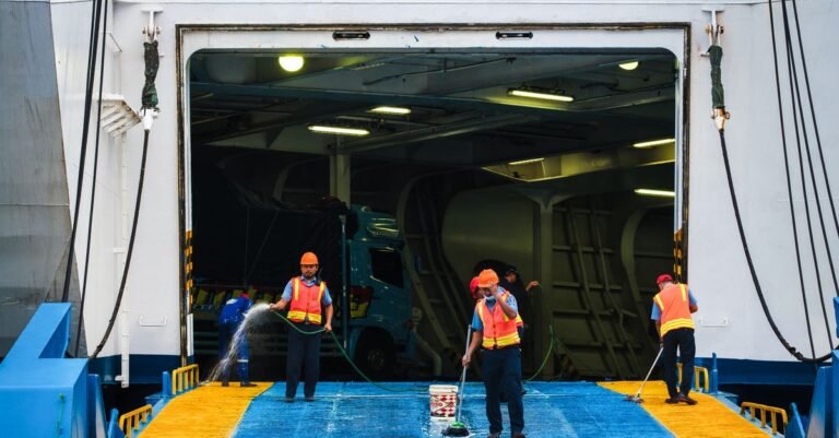 Workers dragging high-pressure hoses while washing down a ferry ramp at a port
